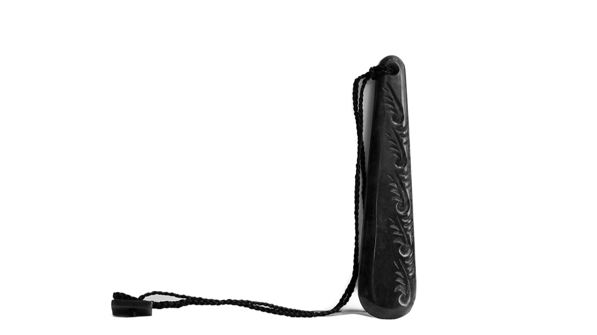 High-key black and white study of a carved pounamu toki pendant